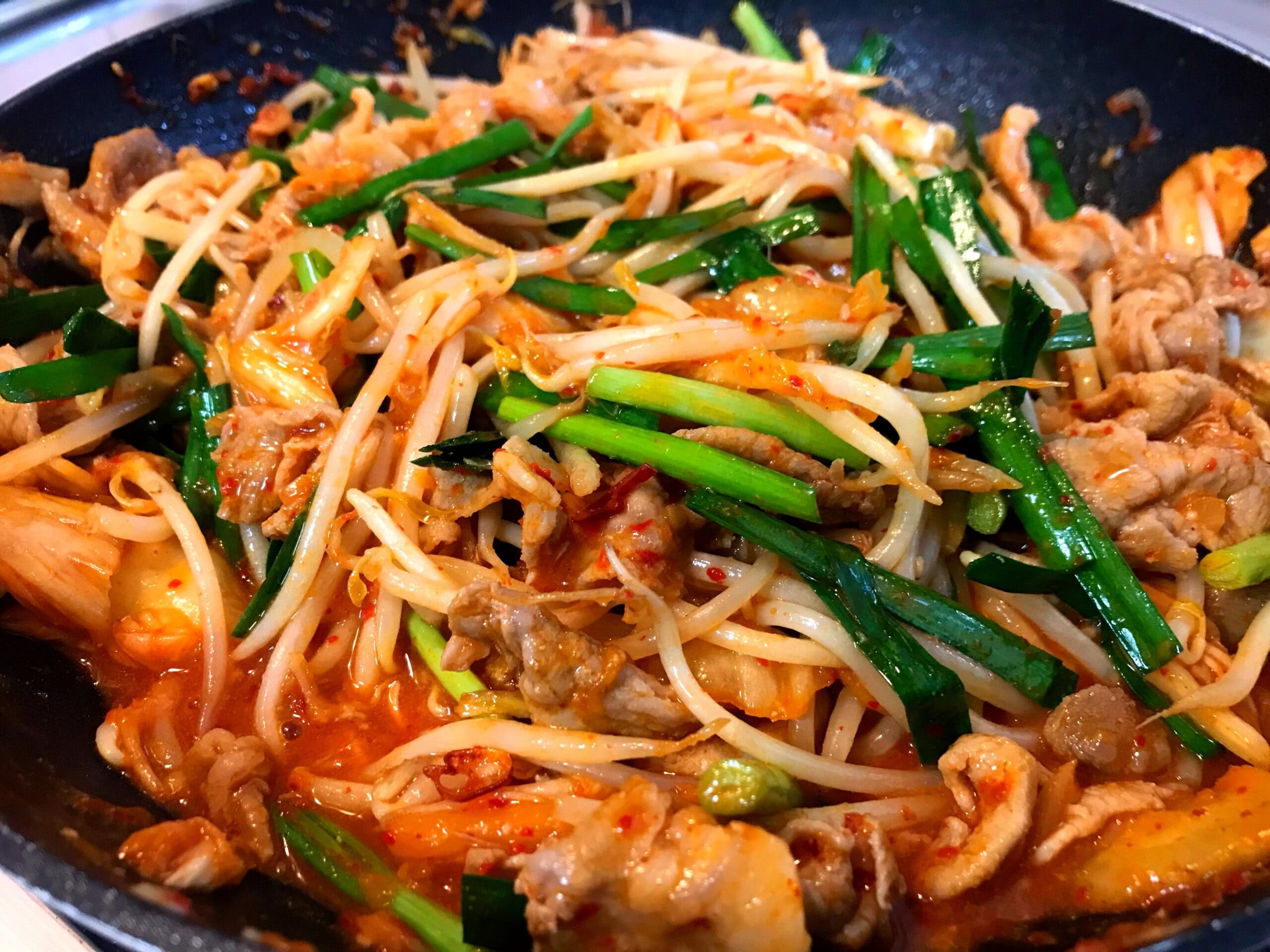 豚肉とキムチ、もやし、ニラをフライパンで炒めている調理中の様子