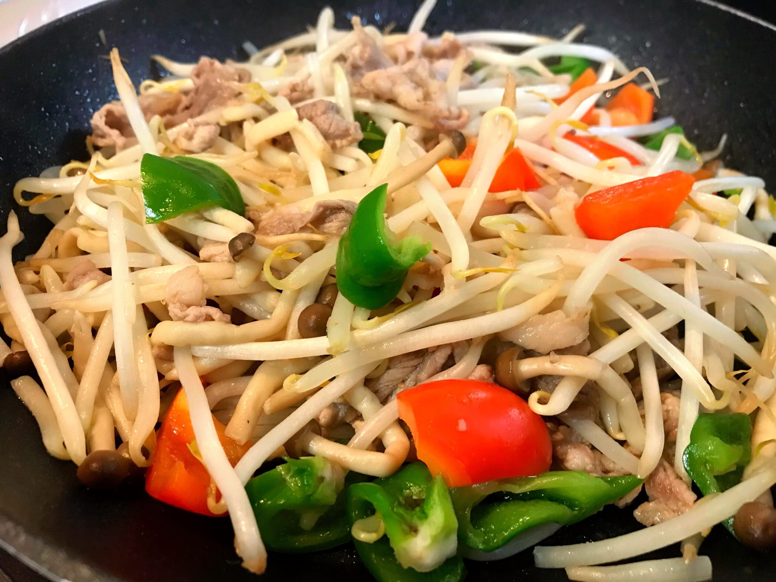 フライパンで豚肉ともやし、ピーマンをガリバタ醤油で炒めている調理中の写真