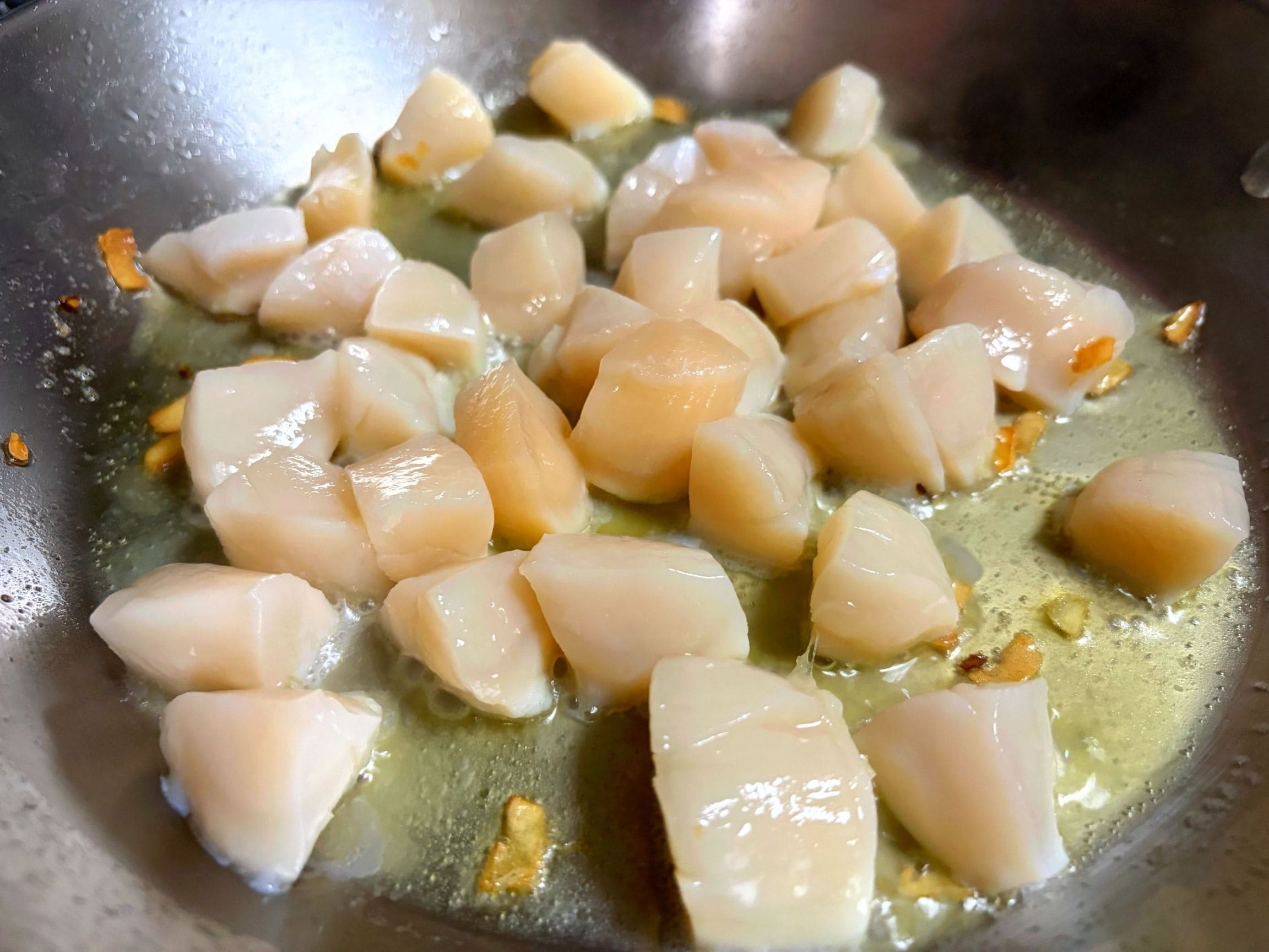 みじん切りにしたニンニクと４等分に切ったホタテをオリーブオイルでソテーしている様子