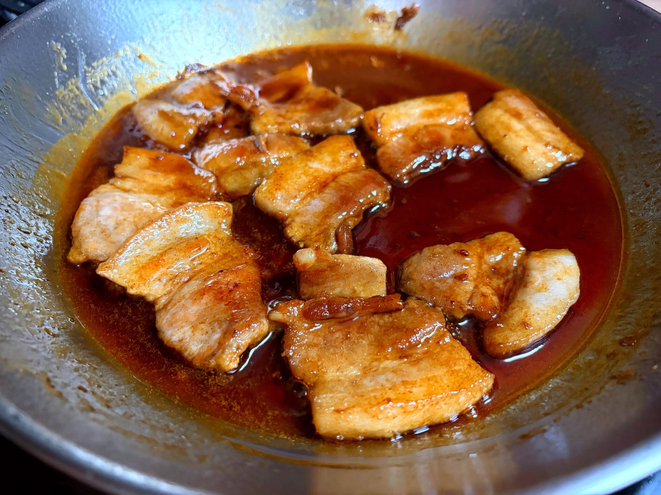 フライパンで豚肉にニンニク醤油ダレを加え、火を入れて味をなじませている様子