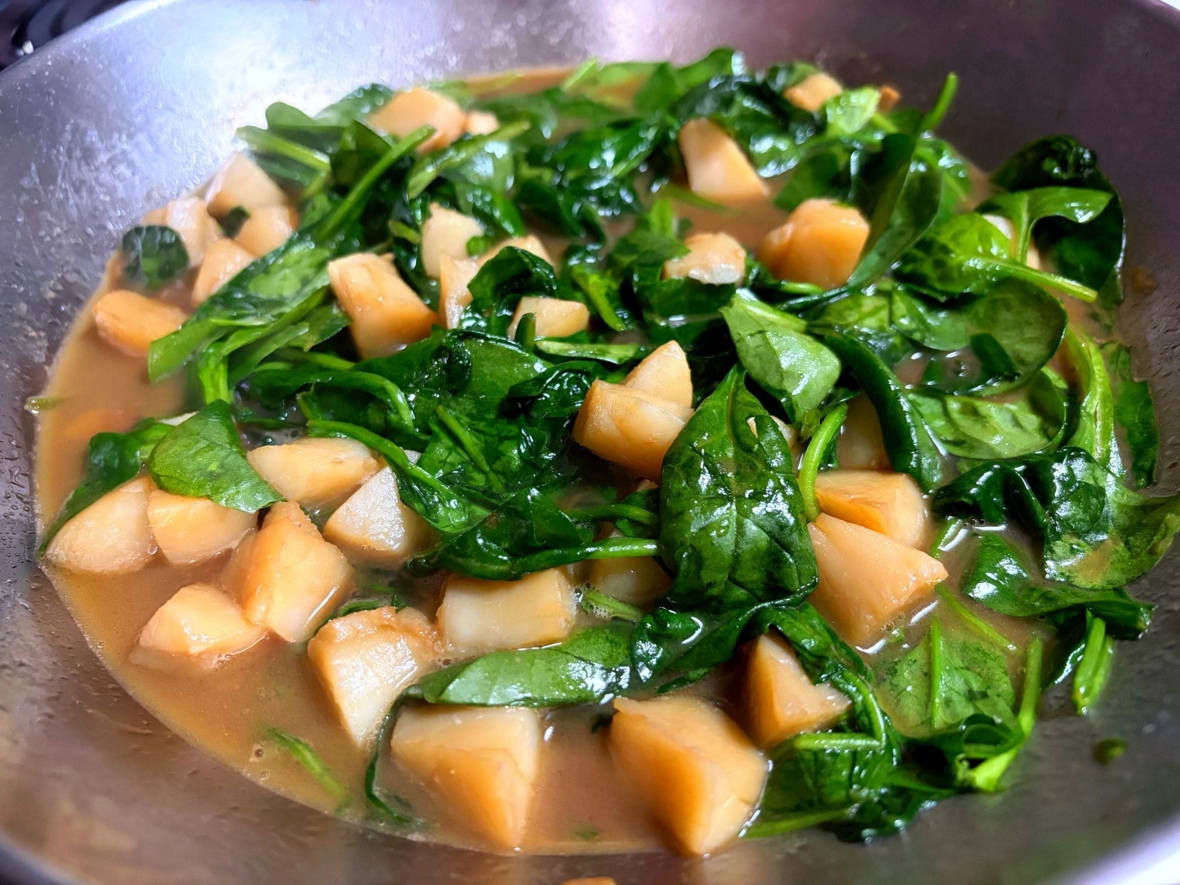 ソテーした一口大のホタテとベビーほうれん草を、ガーリックバター醤油のソースで煮絡めている様子