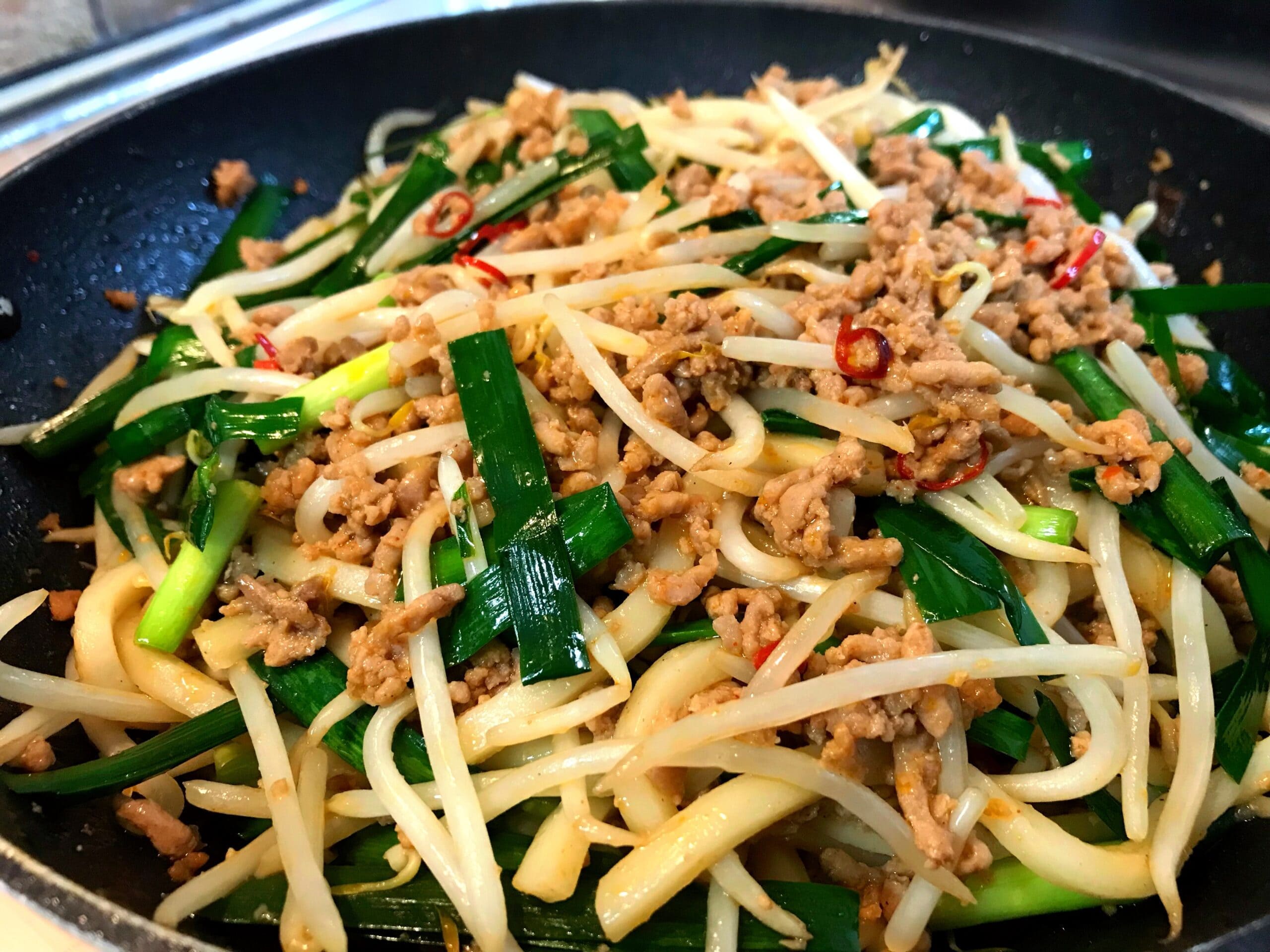 ニラともやし、豚ひき肉をフライパンで炒めている台湾焼うどんの調理工程