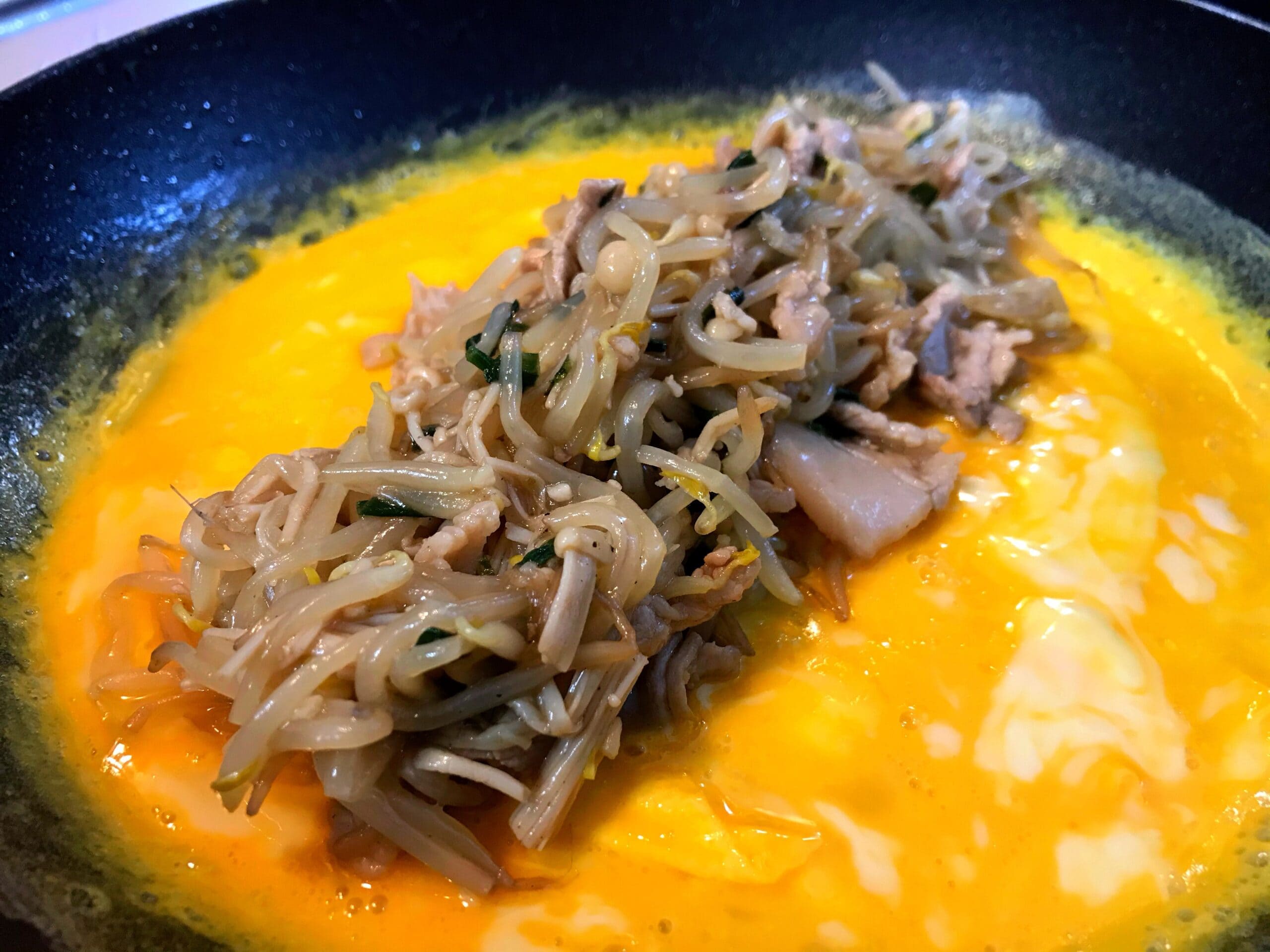 溶き卵の上にもやしと豚肉の炒め物をのせたとんぺい焼き工程