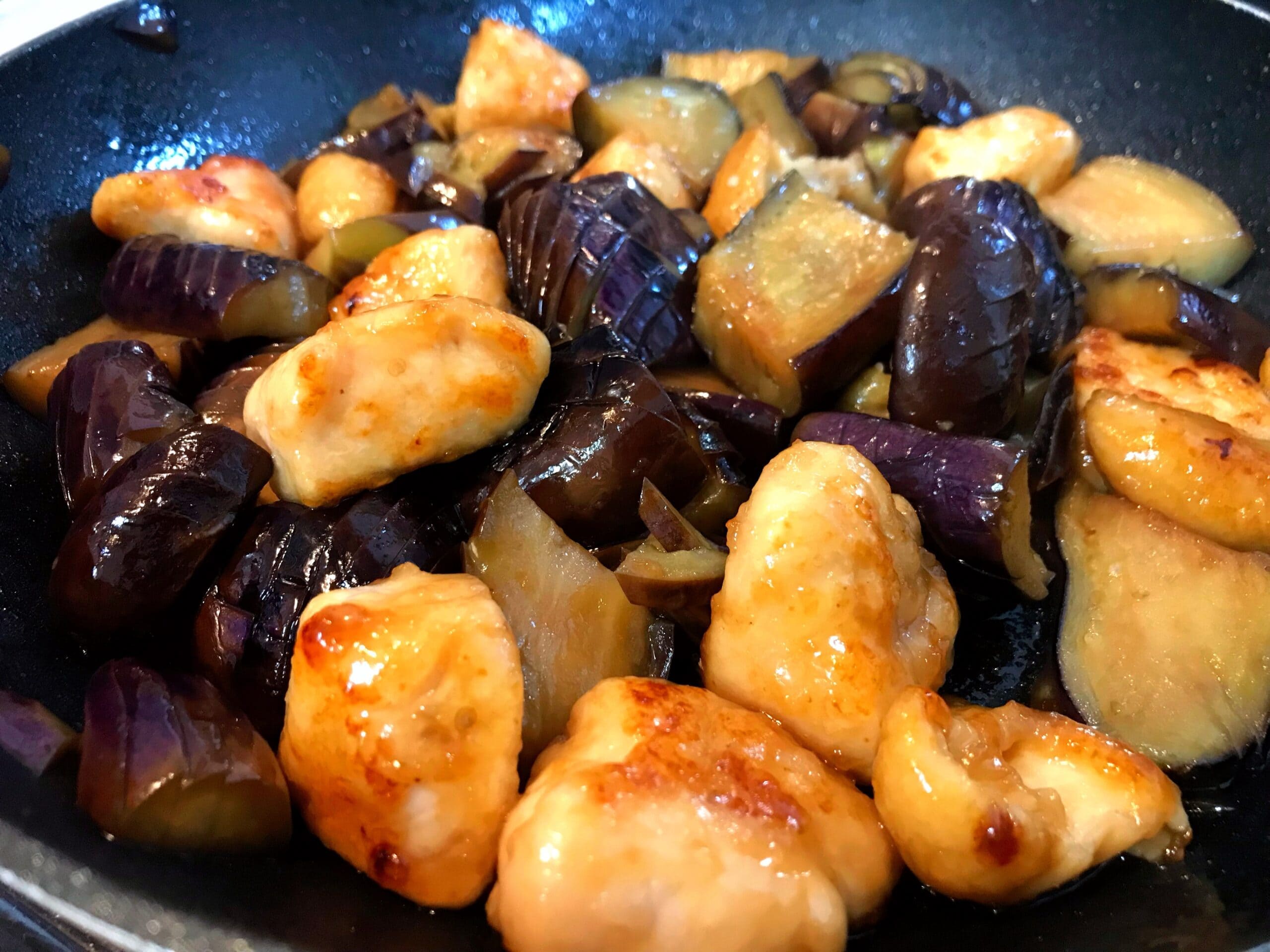 フライパンで茄子と鶏むね肉を甘酢だれで炒めている様子。鶏むね肉がしっとり焼き上がっている
