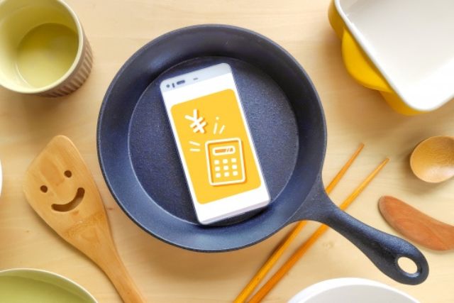 フライパンとスマートフォンの電卓表示で節約料理をイメージした写真