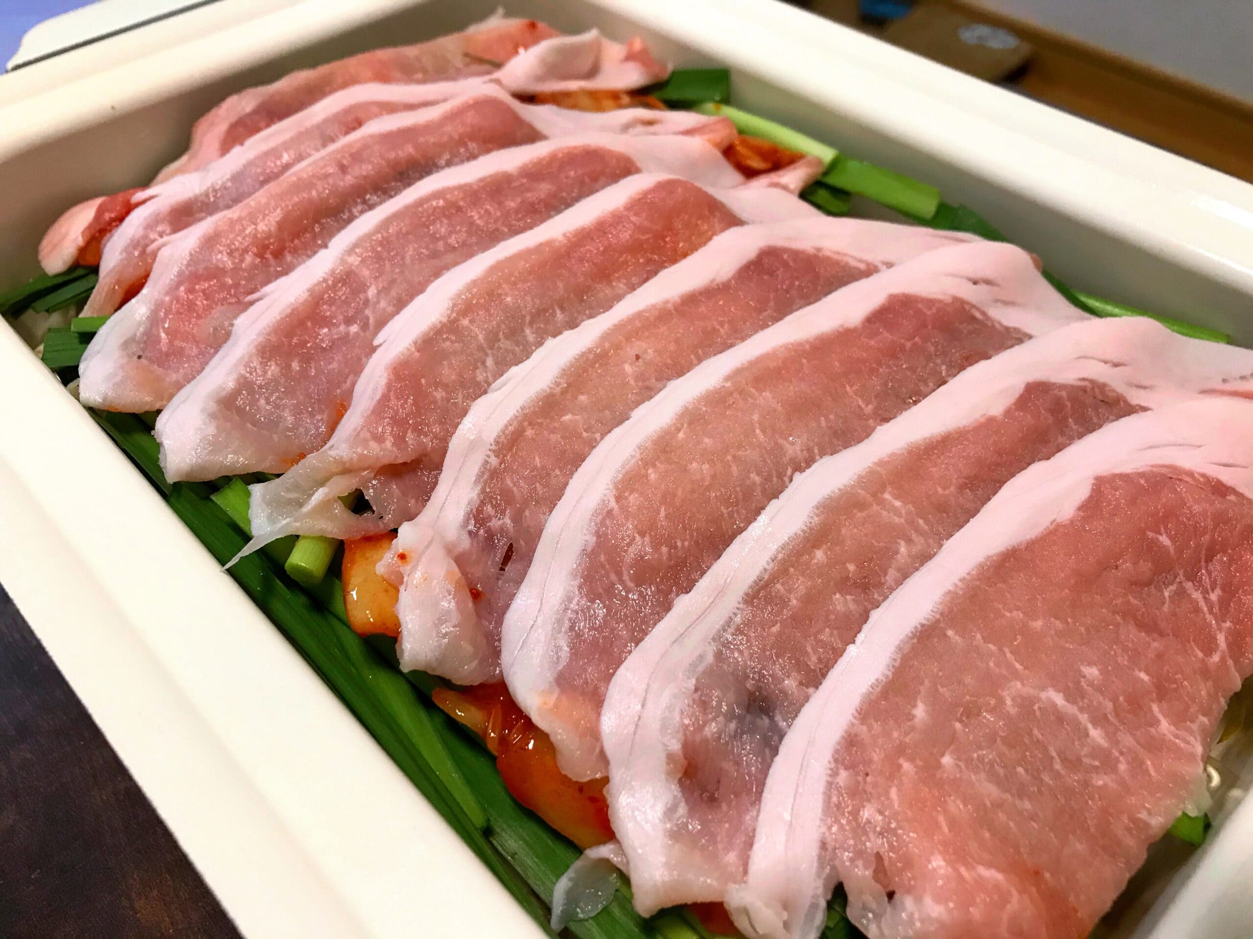 ホットプレートで作るキムチと野菜の上に豚肉を並べた蒸し豚焼肉の調理途中