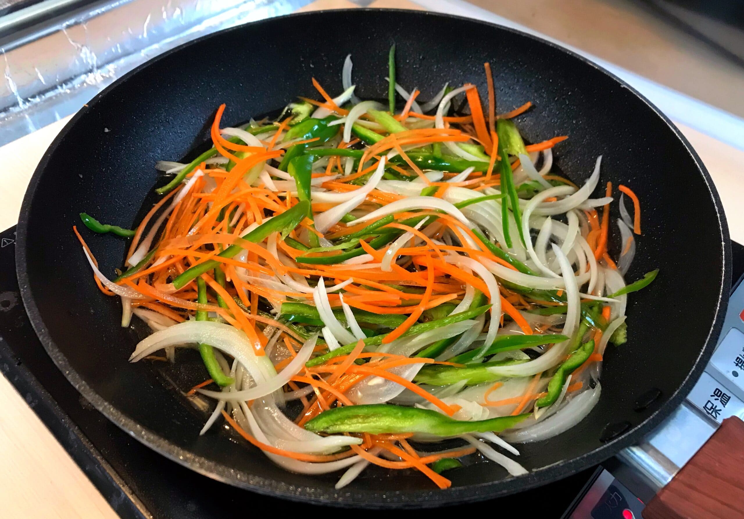 にんじん、玉ねぎ、ピーマンをフライパンで炒めて和風あんかけの具材を作る様子