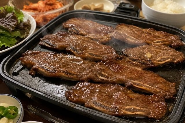 特製タレに漬け込んだLAカルビをホットプレートで香ばしく焼いている調理途中の写真