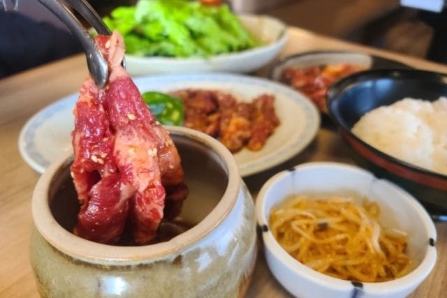 特製タレに漬け込む前のLAカルビを持ち上げ、韓国風焼肉の下ごしらえをしている写真