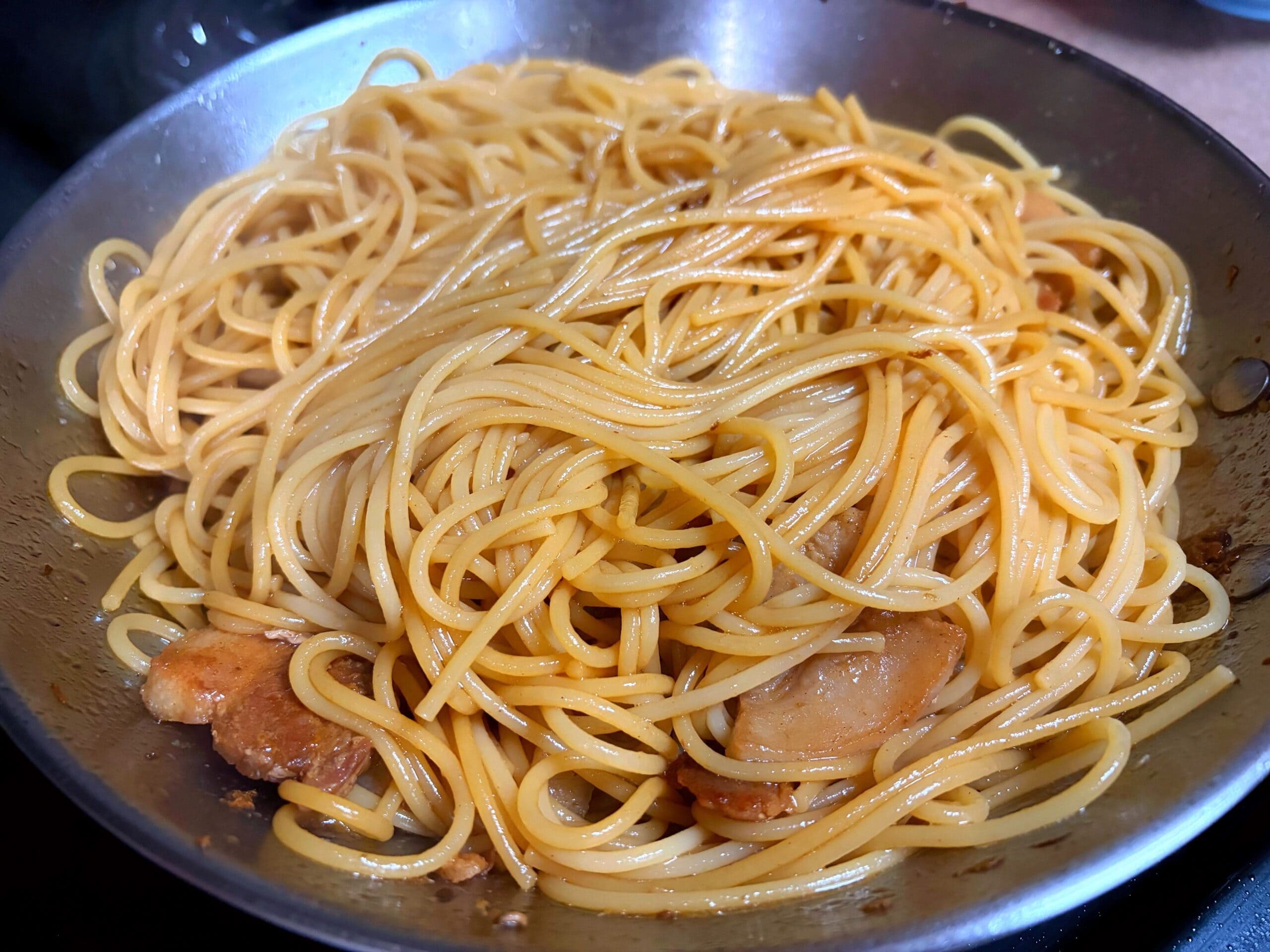 豚ニンニク醤油の野菜マシマシ二郎パスタ用に、茹でたパスタをフライパンに加えて、豚肉の旨味とニンニク醤油ダレを絡めている写真