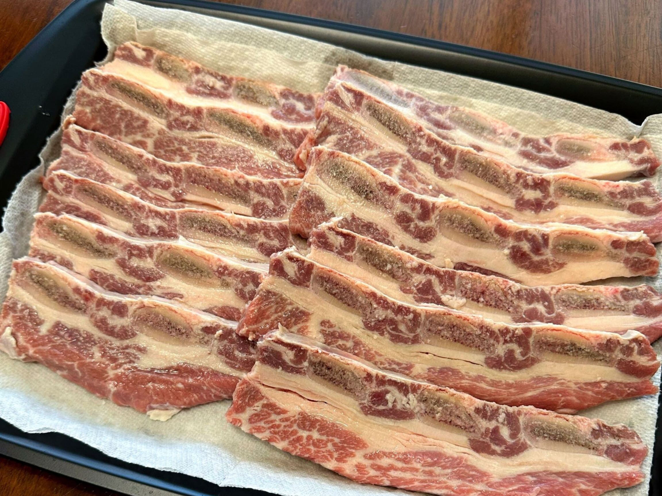 特製タレに漬け込む前の生のLAカルビをトレーに並べた下ごしらえ写真