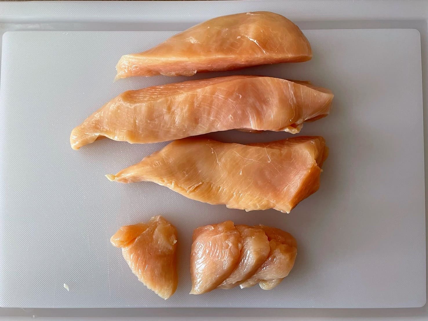 鶏むね肉を縦に切ってからそぎ切りにし、ピリ辛炒め用に下ごしらえしている写真