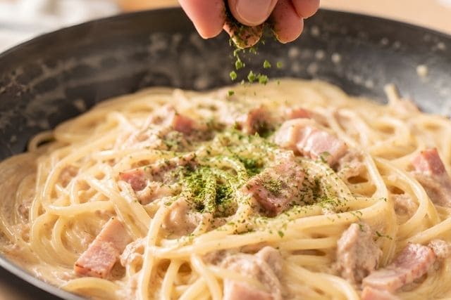 クリームソースとパスタを合わせたあと、仕上げに青のりを加えて香りを引き立てている調理途中の写真