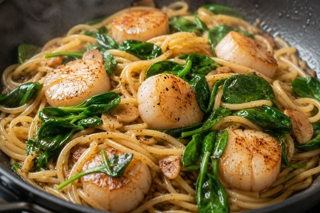 ホタテとパスタにベビーほうれん草を加えて、余熱で色よく仕上げているガリバタ醤油パスタ