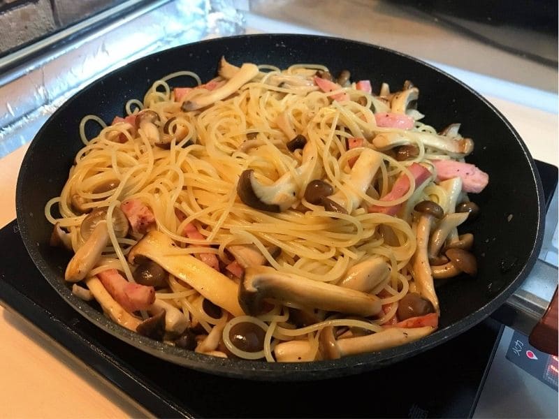 フライパンでベーコン、しめじ、エリンギ、パスタを炒め合わせている和風パスタの調理途中写真