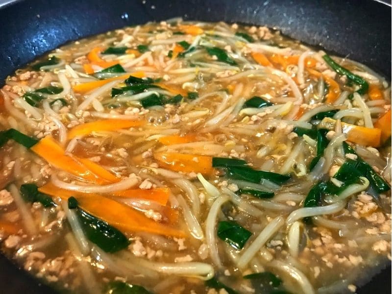 豚ひき肉、もやし、にんじん、ニラを煮て水溶き片栗粉でとろみを付けている調理途中
