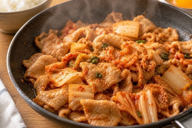 豚キムチ丼を美味しく作るために、豚肉に火を通してからキムチを加え、フライパンでさっと炒めている写真。