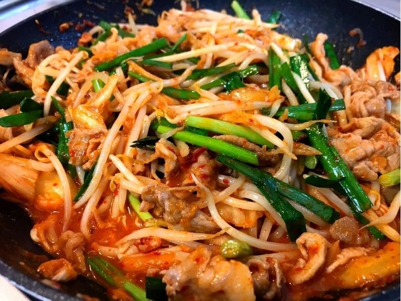 フライパンで豚こま切れ肉、キムチ、もやし、ニラを炒めている豚キムチ丼の調理途中の写真。