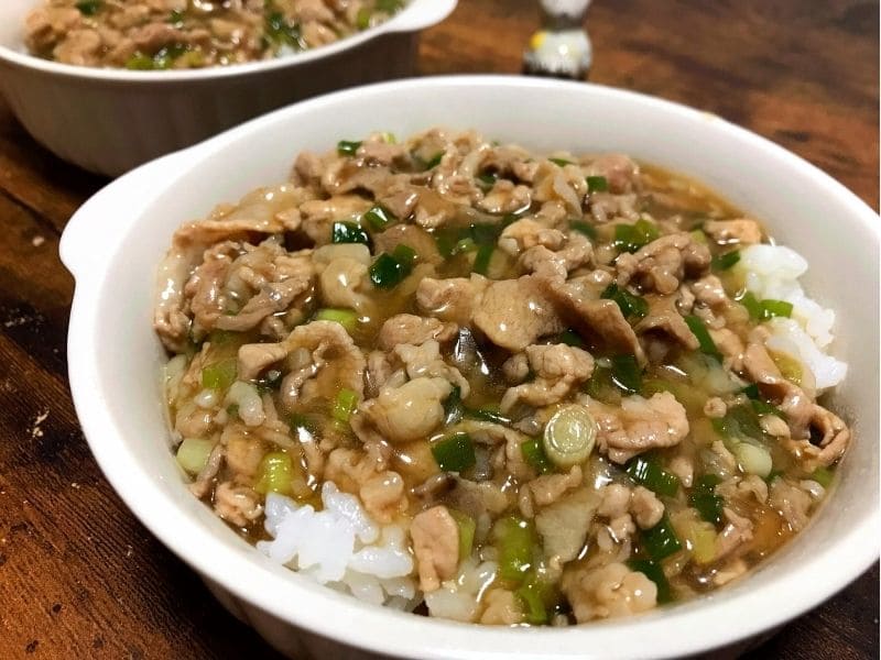 白い器に盛ったごはんに、豚こま肉と長ネギのとろみあんをたっぷりかけた豚こま肉あんかけ丼