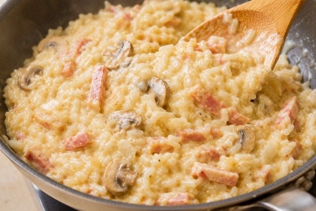 フライパンでチキンラーメンとごはんをカルボナーラソース、ハム、マッシュルームと混ぜている調理途中の写真