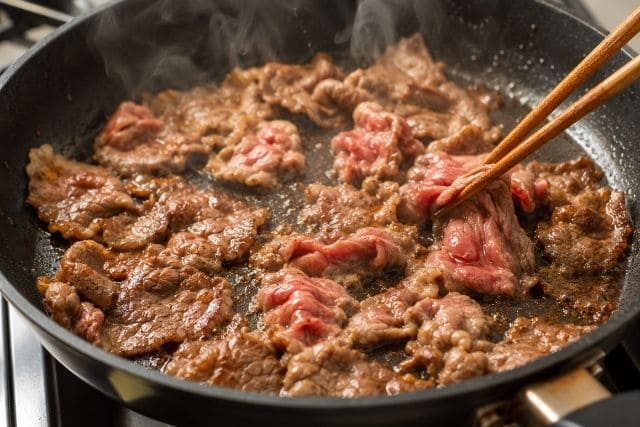 フライパンで薄切り牛肉を炒めているビーフペッパーライスの作り方。牛肉に焼き色をつけて香ばしく仕上げる工程。