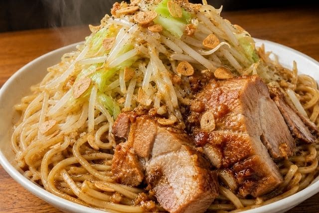 豚ニンニク醤油の野菜マシマシ二郎パスタを、豚肉ともやし、キャベツをたっぷりのせて盛り付けた写真