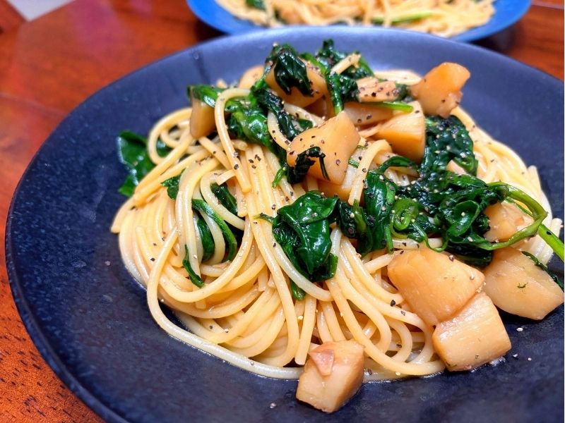 ホタテとベビーほうれん草を使ったガリバタ醤油味の和風パスタを黒い皿に盛り付けた写真