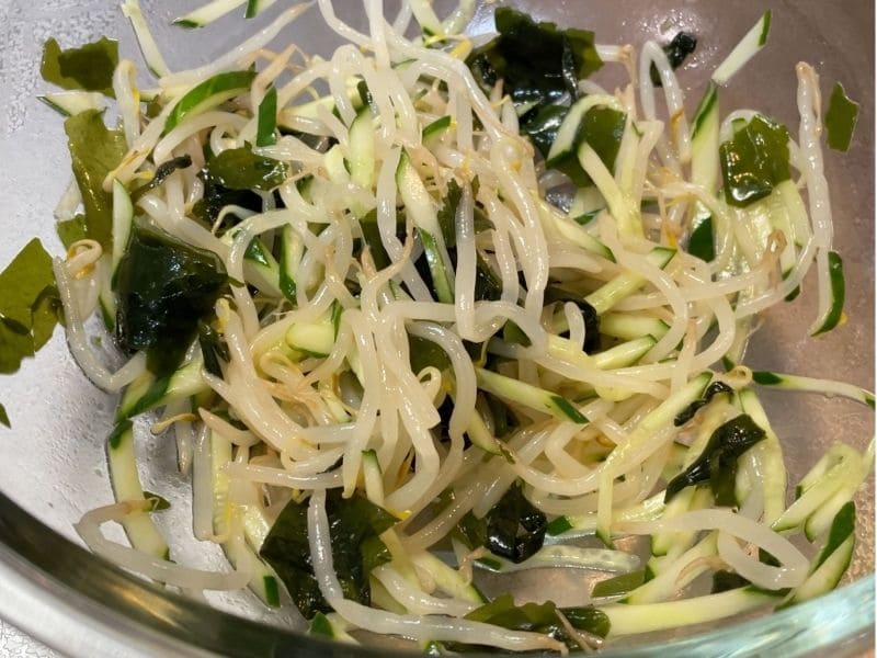 ボウルでもやし、きゅうり、わかめを鶏ガラスープの素とごま油で混ぜ合わせる、もやしナムルの調理途中。