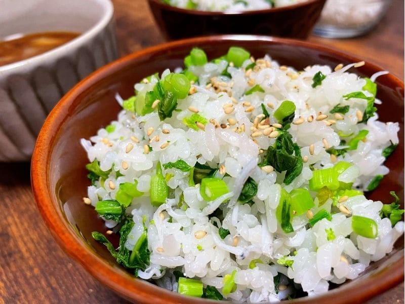 茶色い器に盛り付けた菜の花と釜揚げしらすの混ぜごはん、白いりごまを散らした春の簡単和風レシピ