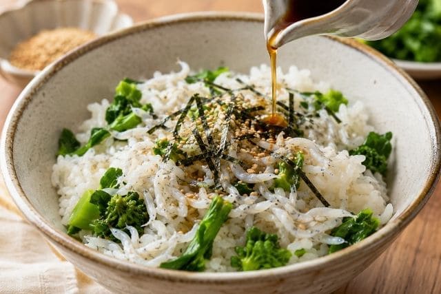 菜の花と釜揚げしらすの混ぜごはんに醤油を少し加え、刻み海苔と白ごまで風味を足す工程