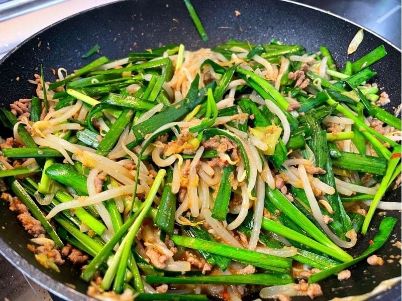 フライパンでニラ、もやし、長ネギ、豚ひき肉を炒めて担々炒めを作っている調理途中の写真