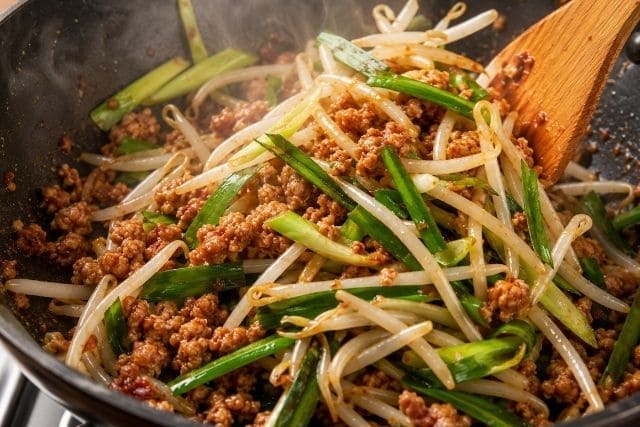 フライパンでニラ、もやし、長ネギ、豚ひき肉を炒めて担々風のピリ辛おかずを作っている調理途中の写真