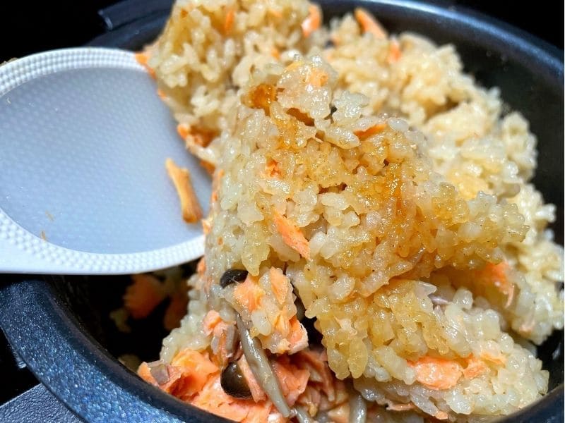 炊飯器で炊いた鮭とキノコのバター醤油炊き込みご飯をしゃもじで混ぜている写真