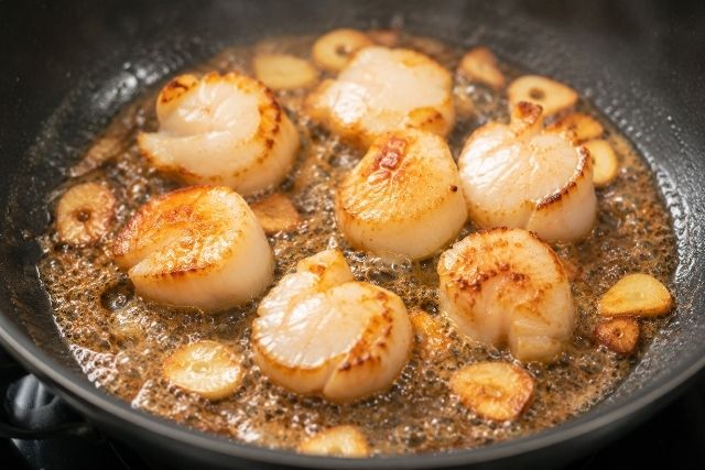 フライパンでホタテをにんにくバター醤油風味に香ばしく焼いている調理