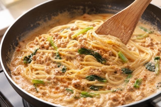 木べらで混ぜながら胡麻ミルクスープをパスタに絡めている様子。ダマにならずクリーミーに仕上げる調理工程