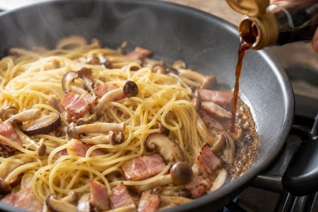 ベーコンときのこの和風パスタに醤油を鍋肌から回し入れて香ばしく仕上げる調理工程写真