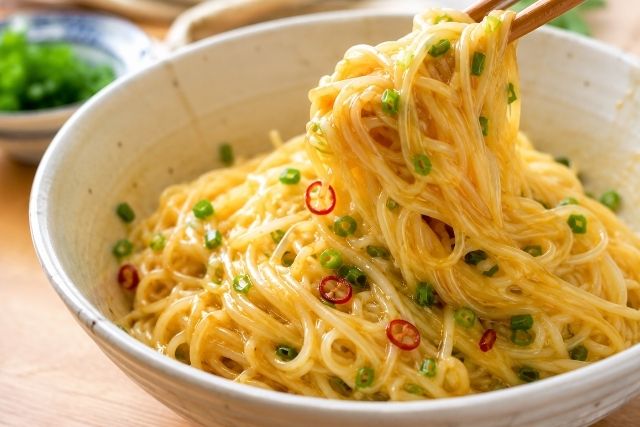 卵黄と小ネギ、輪切り唐辛子を絡めた油そば風そうめんを箸で持ち上げる様子