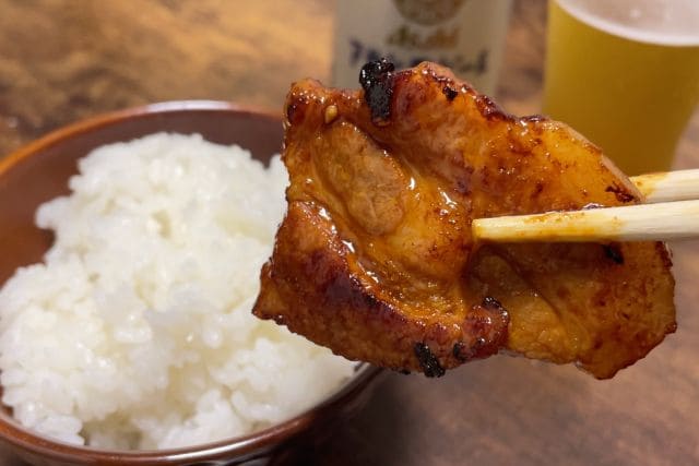 箸で持ち上げた甘辛い味付き豚バラ焼肉と白いご飯