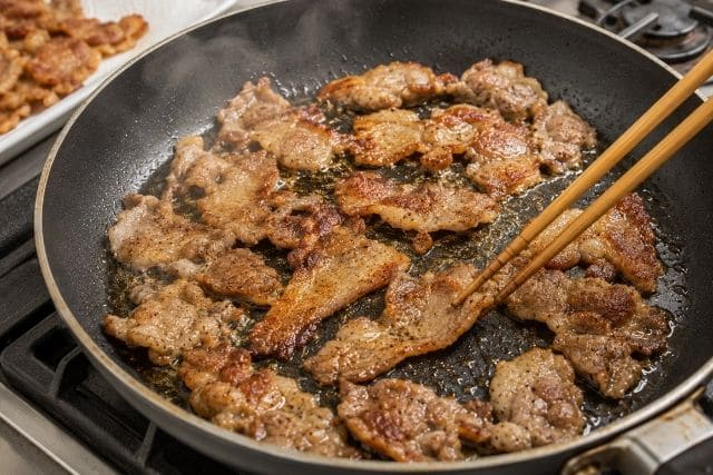 フライパンに豚こま切れ肉を広げ、豚肉から出た脂でカリカリに揚げ焼きする様子