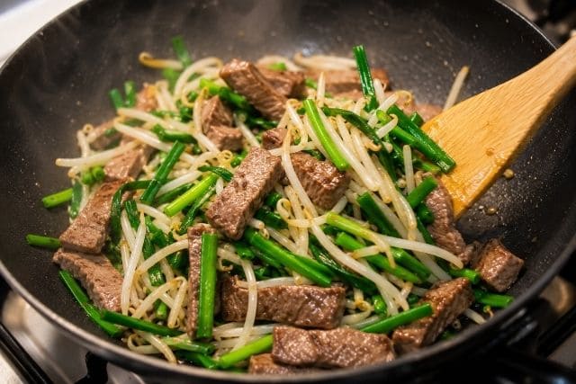 フライパンで牛タンともやしとニラを強火で手早く炒めている様子