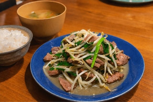 青い皿に盛り付けた牛タンとニラともやしのスタミナ炒めと白いご飯