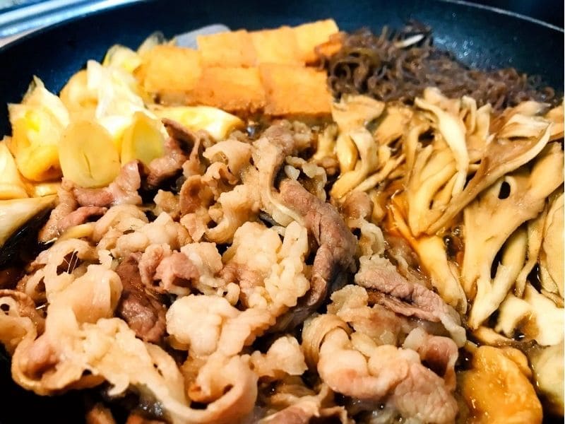 フライパンで牛薄切り肉、厚揚げ、長ネギ、舞茸、糸こんにゃくを甘辛だれで煮込む夏野菜の冷やし牛すき焼きの調理途中