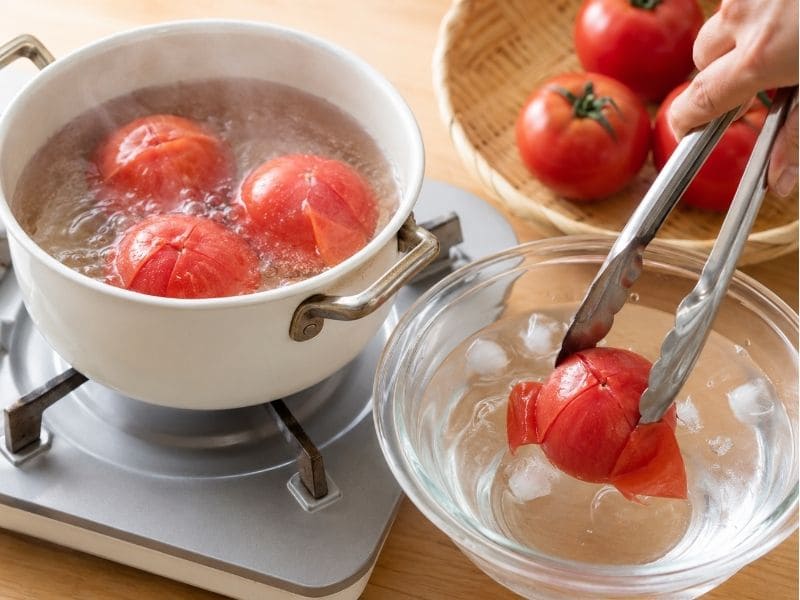 冷やしトマトおでんの作り方で、切り込みを入れたトマトを茹でて冷水にさらしている調理途中の写真