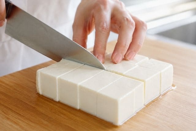 釜揚げしらすと薬味の豆腐サラダ用に絹ごし豆腐を包丁で切り分けている様子