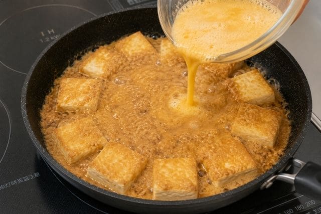 こんがり焼いた木綿豆腐に長芋と卵のとろろタネを流し入れている様子