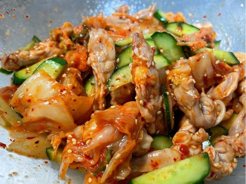 茹でたせせり、きゅうり、白菜キムチをごま油と白いりごまで和えている調理途中