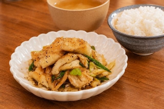 白い器に盛り付けた白身魚と長ネギのバタぽん炒めと白いご飯、汁物