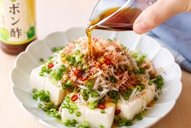 釜揚げしらすと小ネギ、かつお節をのせた豆腐サラダにポン酢を回しかけている様子
