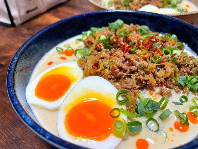 青い器に盛り付けたピリ辛豚ひき肉の豆乳ごまそうめんに、半熟卵と小ネギ、輪切り唐辛子をトッピング