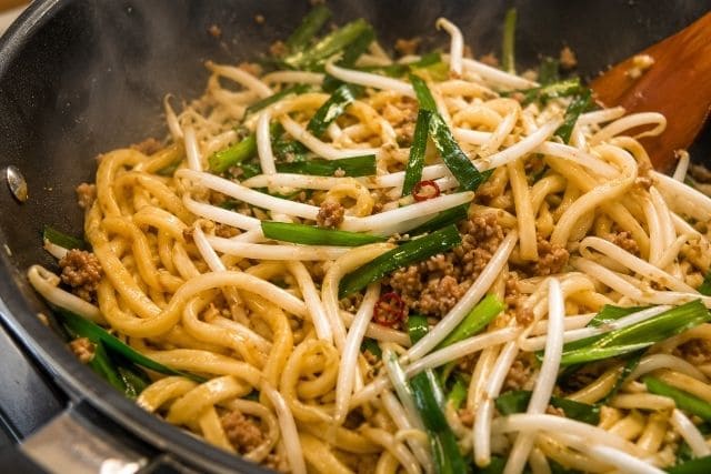 豚ひき肉入りの焼うどんにニラともやしを加え、食感を残すように炒めている写真